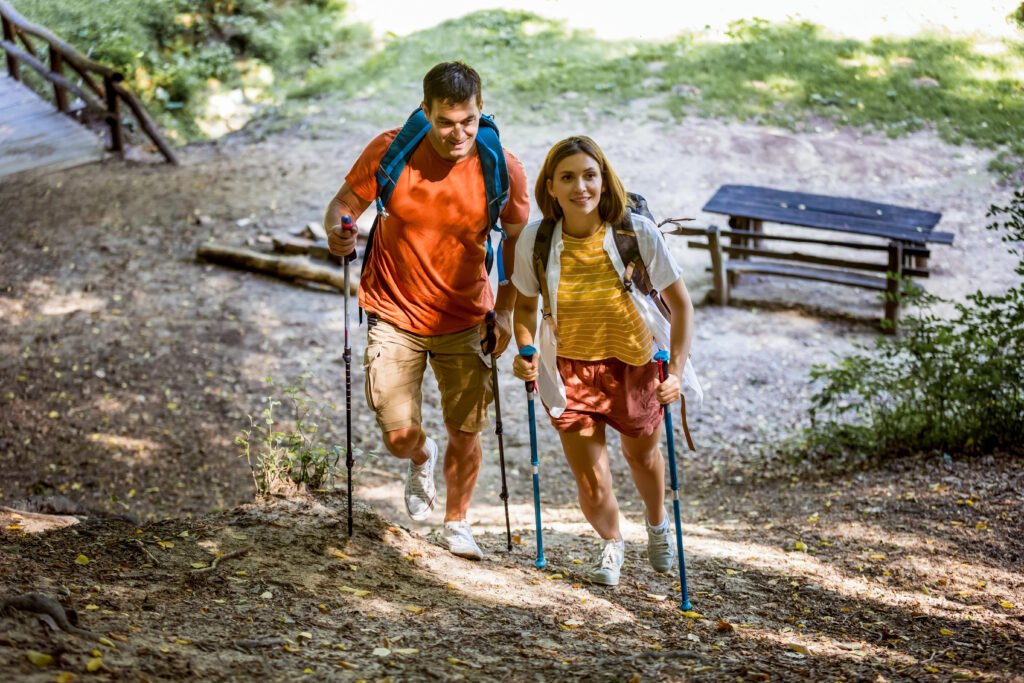 Married couple hiking through a forest with hiking poles and backpacks